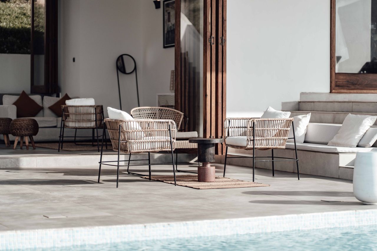 Luxurious outdoor seating area by the pool with modern wicker chairs and soft cushions.